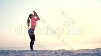 健康的年轻美女，日出时在海边打坐，伸展身体，练习瑜伽